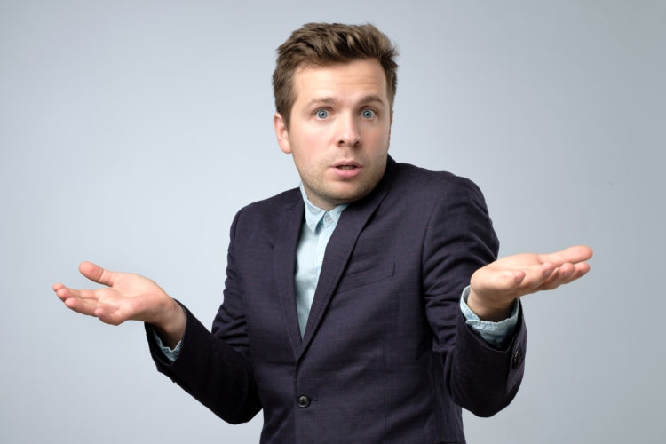 Confused young caucasian man in suit shrugging his shoulders.