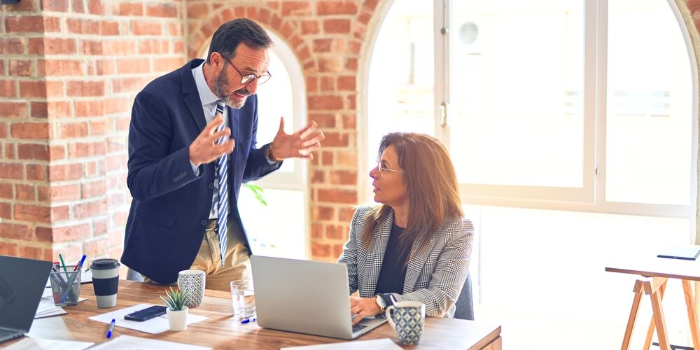 Two middle age business workers working together. Man bullying woman at the office
